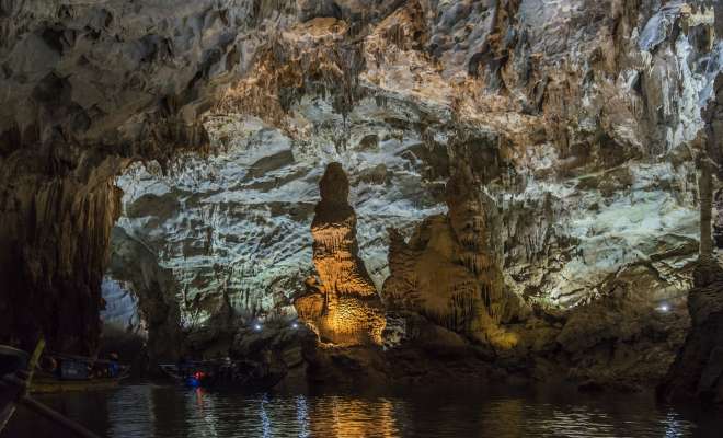 Boats row slowly along a river in a huge cavern in a vast limestone cave near Phong Nha