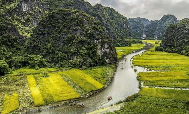 Small boats carry visitors along waterways threading between cliffs and rice fields