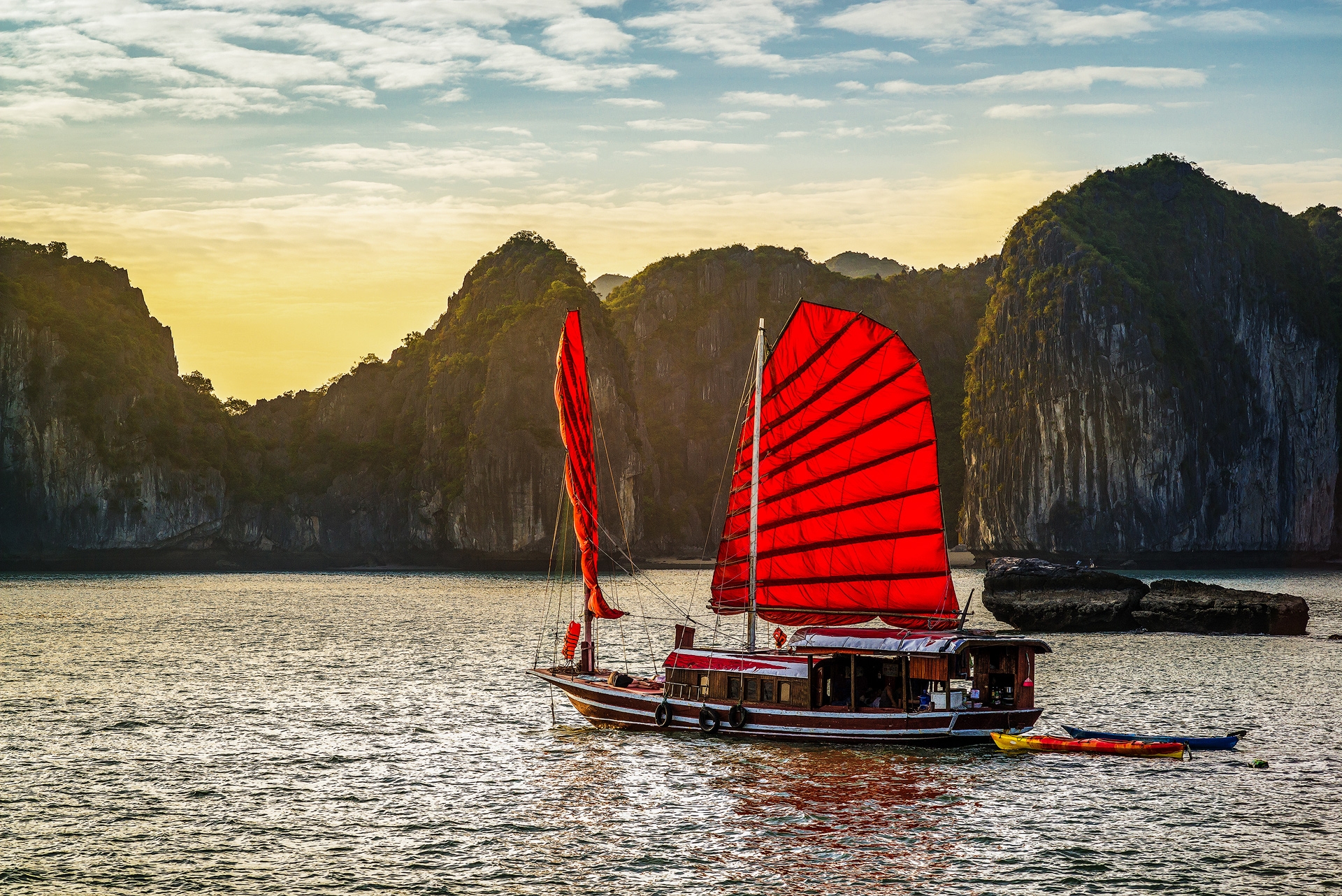Ha Long Lan Ha Bay - small junk with red sails and sunset cliffs behind